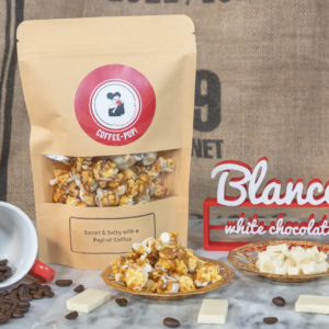 Coffee-flavored popcorn with white chocolate on a marble surface, surrounded by coffee beans and a decorative sign.